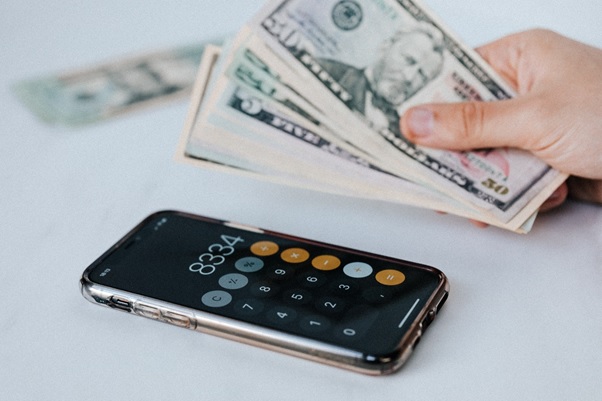 A person holding cash in their hand next to an iPhone with the calculator app open